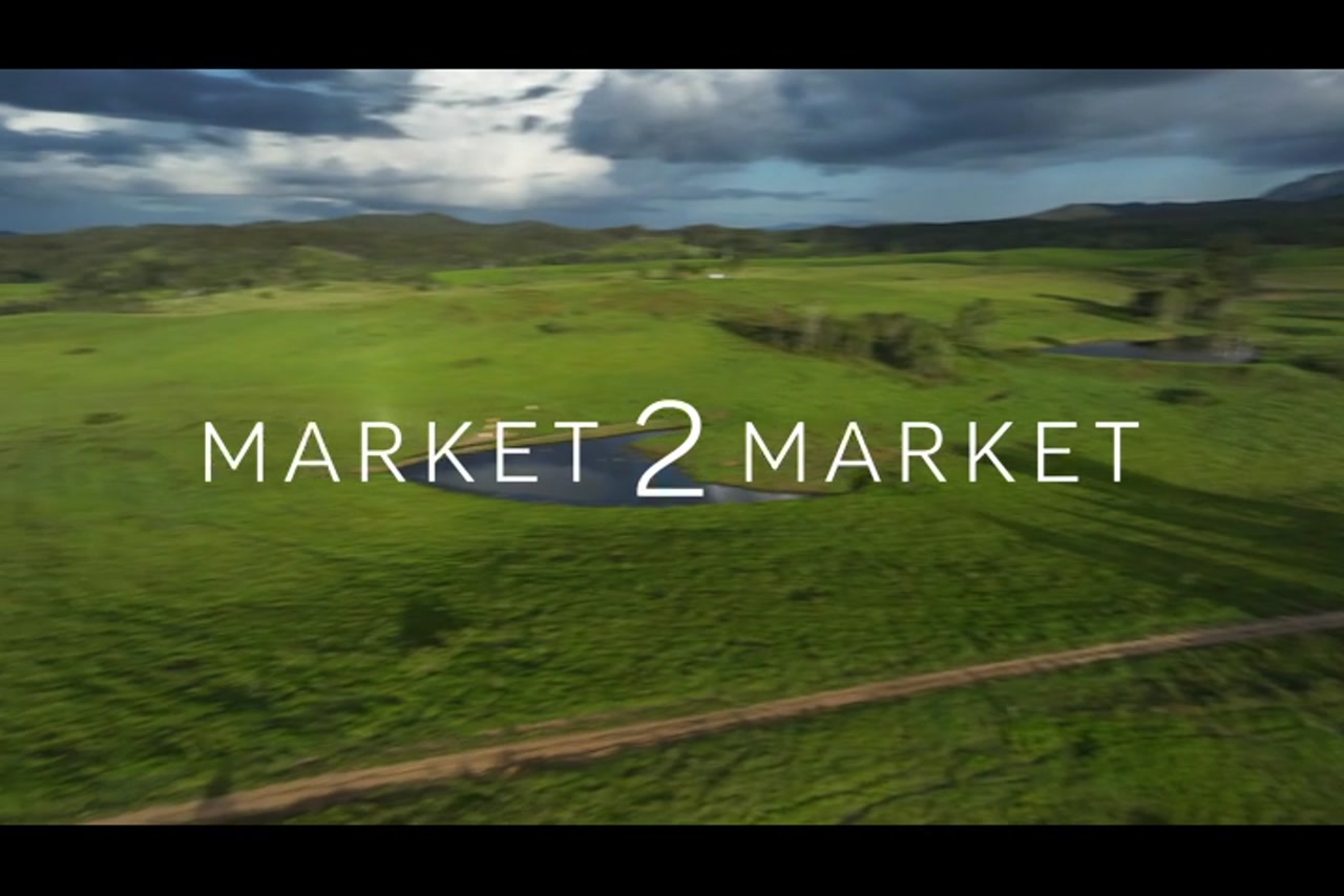 Aerial footage over a kubota driving down dirt track in lush, green farmland with a small dam